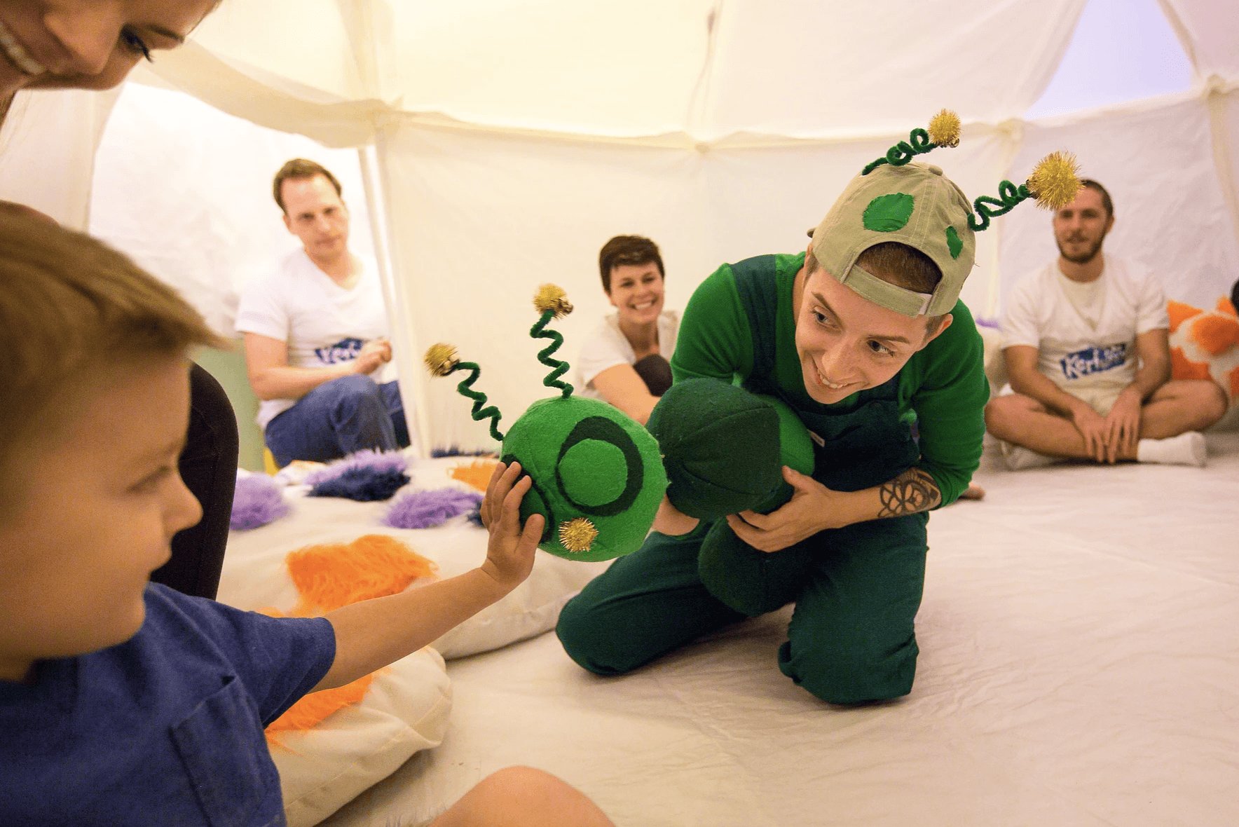 Image of performer in a green costume from A Very Hungry Caterpillar introducing the caterpillar puppet to a young boy.