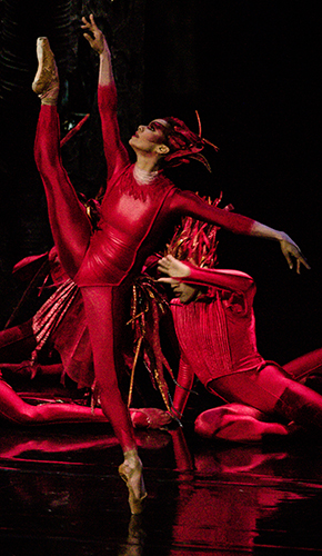 Image of Misty Copeland dressed all in red dancing "Firebird"  in front of two other performers in red seated on the stage