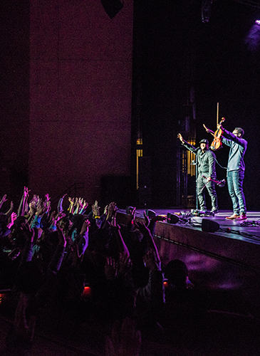 Image of UNL students in the audience applauding and the performers from Black Violin waving to the crowd