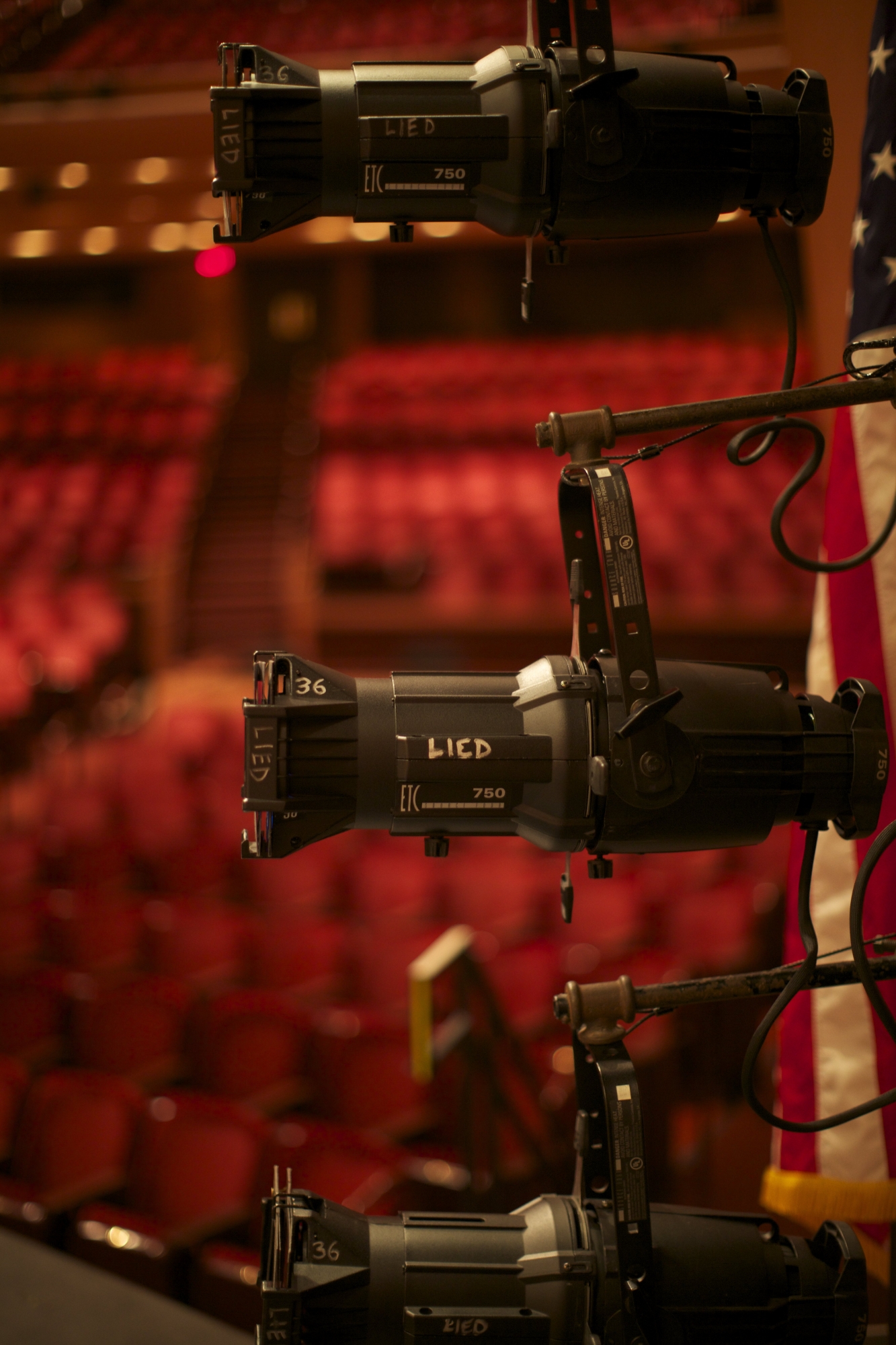 Image of a stage light in the foreground and the iconic red seats of the Lied Center visible in the background