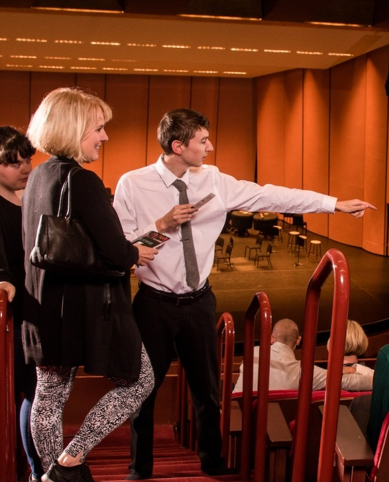 photo of an usher wearing a white shirt directing a woman with blonde hair to her seat.