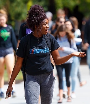 Image of a college student in a black t-shirt and blue jeans walking outside