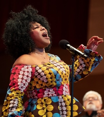 a woman in a colorful dress sings passionately into a microphone