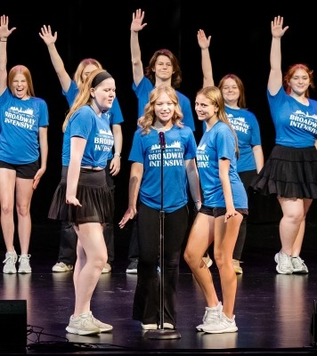 three soloists in blue shirts sing at a microphone