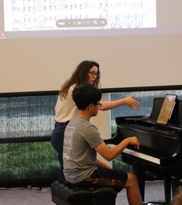 a student plays piano under the tutelage of a teacher