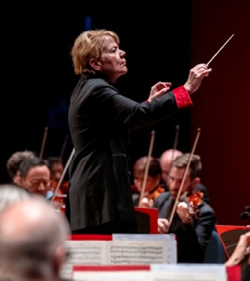 A woman in black conducting an orchestra