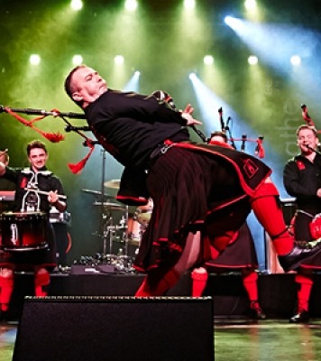 Man playing bagpipes on a stage with green and white stage lights