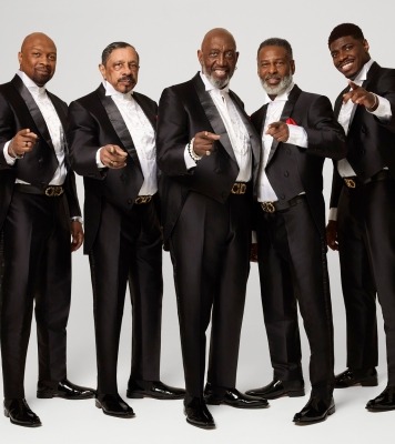 five men in black tuxedos looking suave and pointing to the camera