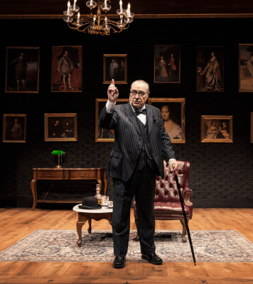 a senior man stands and points while leaning on a cane in an elegant library