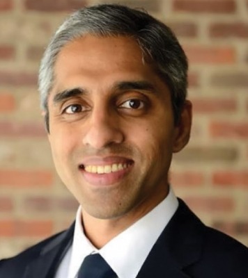 a smiling man in a classy suit gazes into the camera against a brick wall background