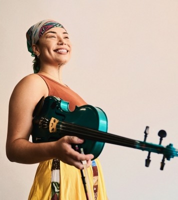 a woman in a colorful dress holds her violin, smiling