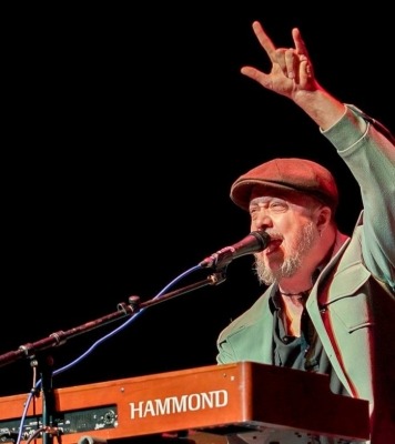 a man in a green jacket and hat plays the keyboard