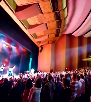 Side view of a packed theater with singers on stage and colorful lights