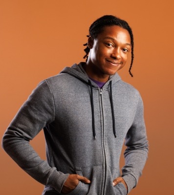 a man poses in a grey hoodie with hands in pockets and a cheeky smile