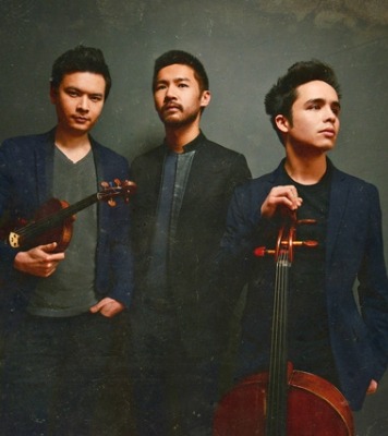 three men pose with instruments in front of a dark and moody background