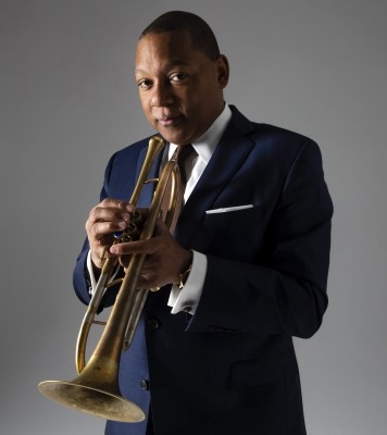 Man holding a trumpet and looking at the camera in front of a grey background