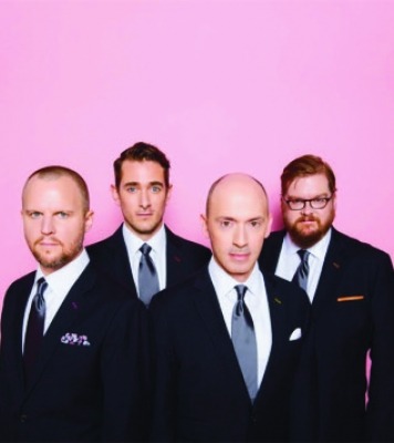 a quartet of men in fancy suits pose in front of a purple-pink background