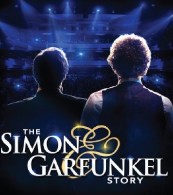 Two men facing away from the camera on a stage with blue lights shining onto the stage. Text at the bottom of the stage reads "The Simon & Garfunkel Story"