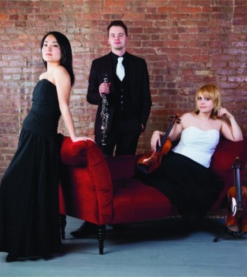three humans in fancy attire pose together on a small red couch