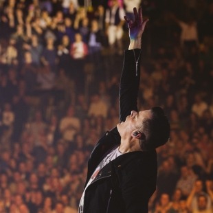 a man onstage poses with one arm raised to the sky