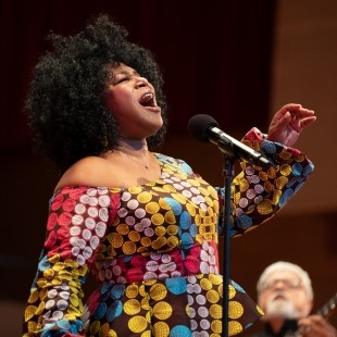 a woman in a colorful dress sings passionately into a microphone