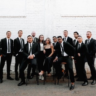 a group of humans dressed in black suits and dresses pose together