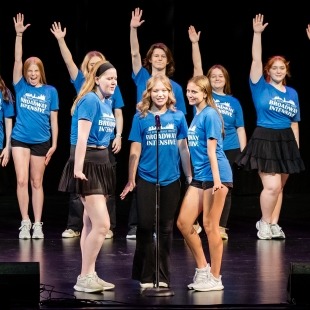 three soloists in blue shirts sing at a microphone