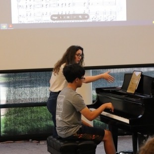 a student plays piano under the tutelage of a teacher
