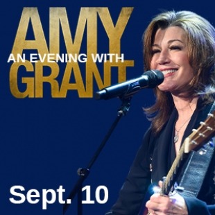 A woman with brown hair and a guitar singing into a microphone with "An Evening with Amy Grant" in gold and white letters
