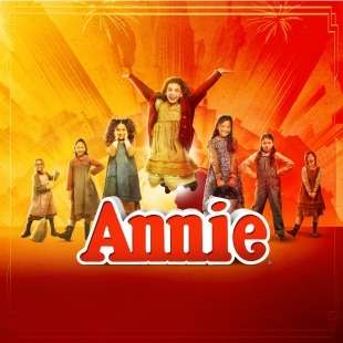 The word Annie with seven girls standing in a V formation and the one in the middle jumping throwing her hands in the air