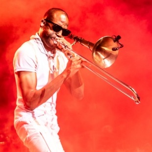 man playing the trombone in sunglasses against a red haze