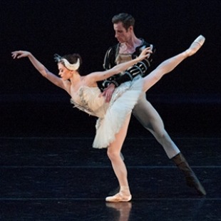 Ballet duo performing a pas de deux; female dancer in white tutu held by male partner on stage.