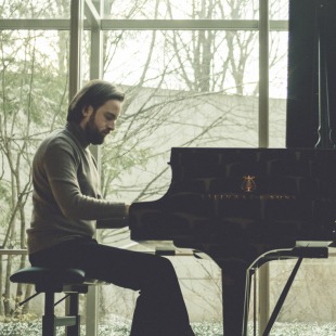 a man sits at a piano in a room with windows for walls