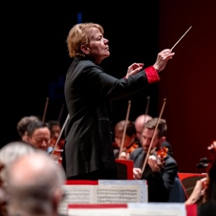 A woman in black conducting an orchestra