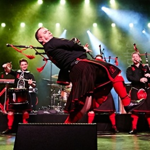 Man playing bagpipes on a stage with green and white stage lights