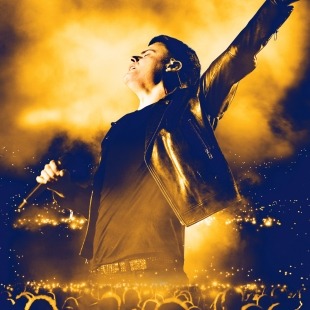 a man onstage poses with one arm raised to the sky
