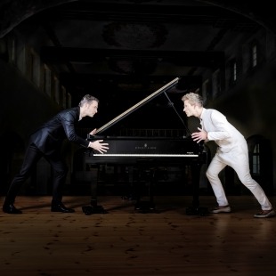 two men face off intensely in front of a piano