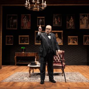 a senior man stands and points while leaning on a cane in an elegant library