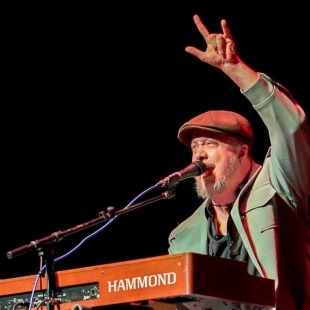 a man in a green jacket and hat plays the keyboard