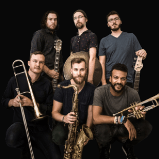 Six men look into the camera. From left to right they hold: A guitar, a cymbal, a bass guitar, a trombone, a tenor saxophone, and a trumpet. 
