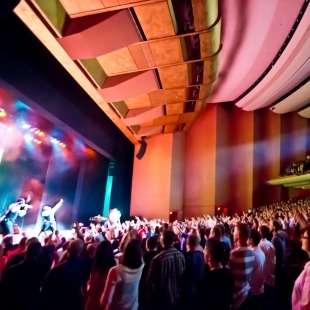 Side view of a packed theater with singers on stage and colorful lights