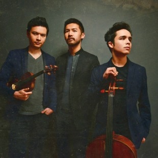 three men pose with instruments in front of a dark and moody background