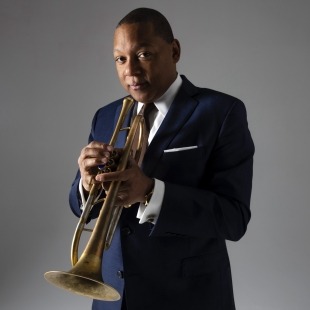 Man holding a trumpet and looking at the camera in front of a grey background