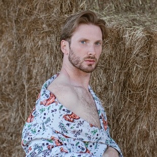 a fashionable man poses in front of hay