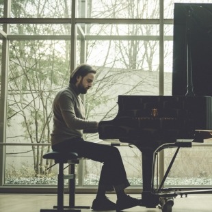 a man sits at a piano in a room with windows for walls