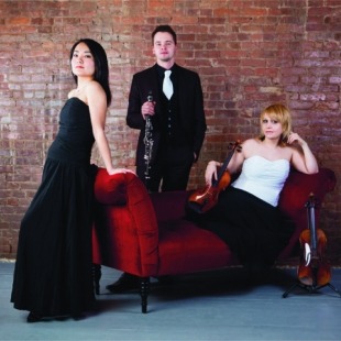 three humans in fancy attire pose together on a small red couch