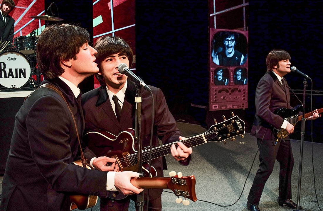 Image of the performers in RAIN on stage in black suits, white, shirts, and black ties in tribute to the early Beatles.
