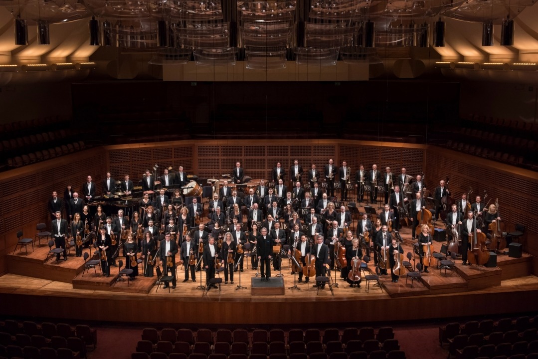 Image of the entire orchestra standing and smiling at the camera