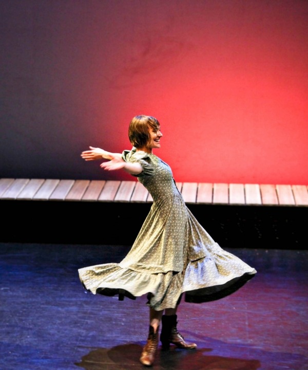 A woman wearing a green dress smiles and twirls