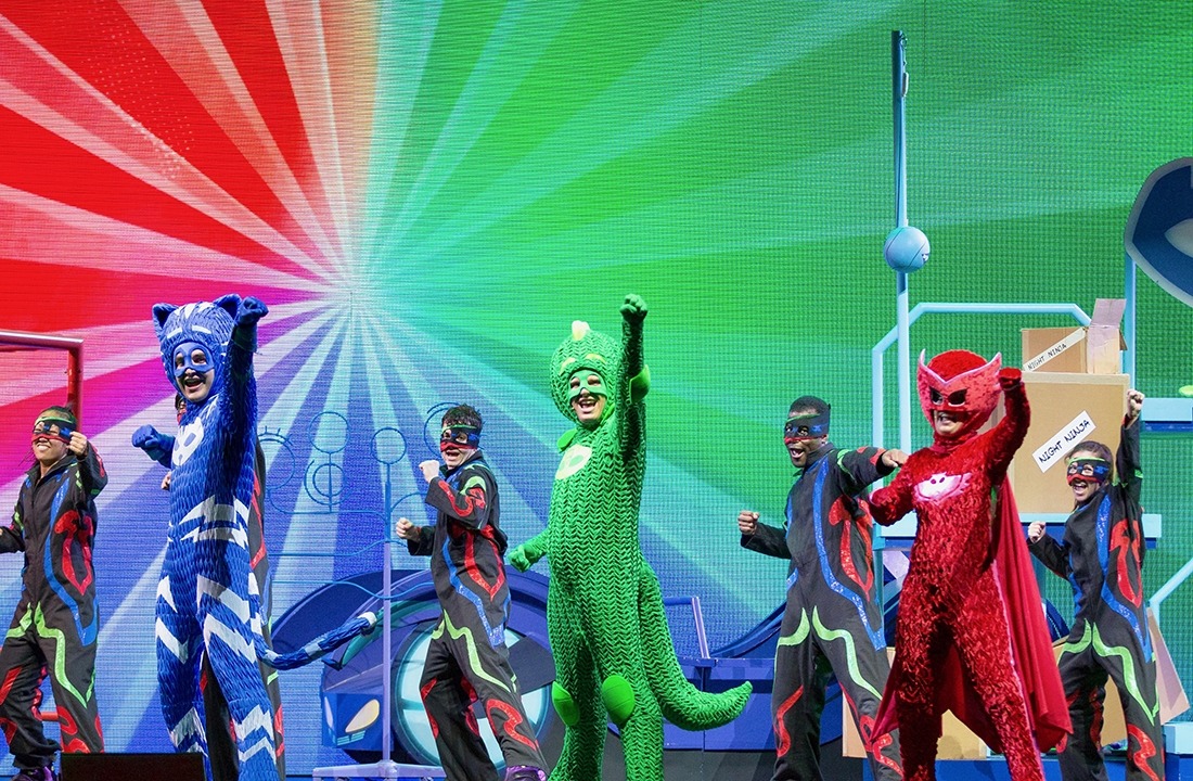 The cast of PJ Masks on stage with one arm raised in the air